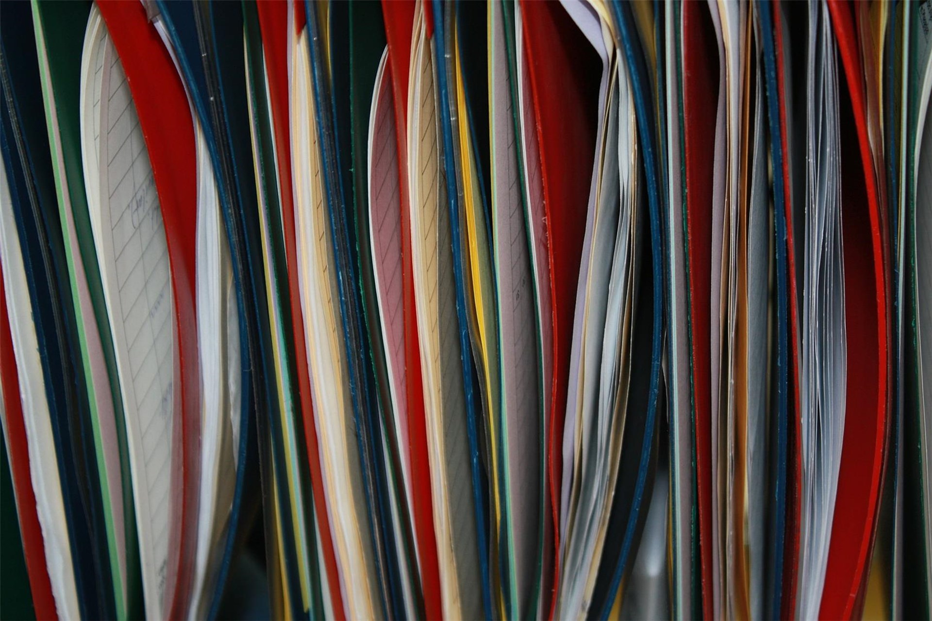 Bunte Aktenordner in verschiedenen Farben, teilweise geöffnet, mit sichtbaren Seiten.