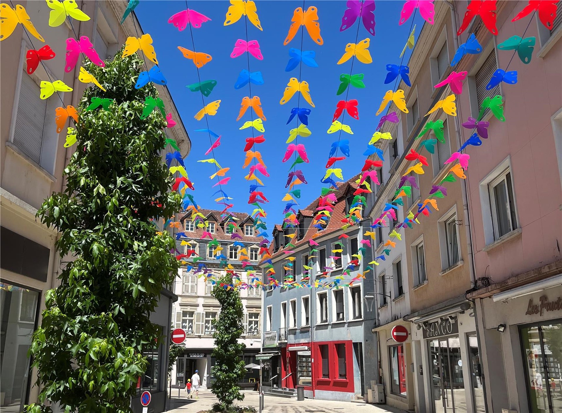 Eine malerische Ansicht einer belebten Straße, geschmückt mit leuchtenden, schmetterlingsförmigen Girlanden, die sich unter einem strahlend blauen Himmel spannen und eine festliche Atmosphäre schaffen