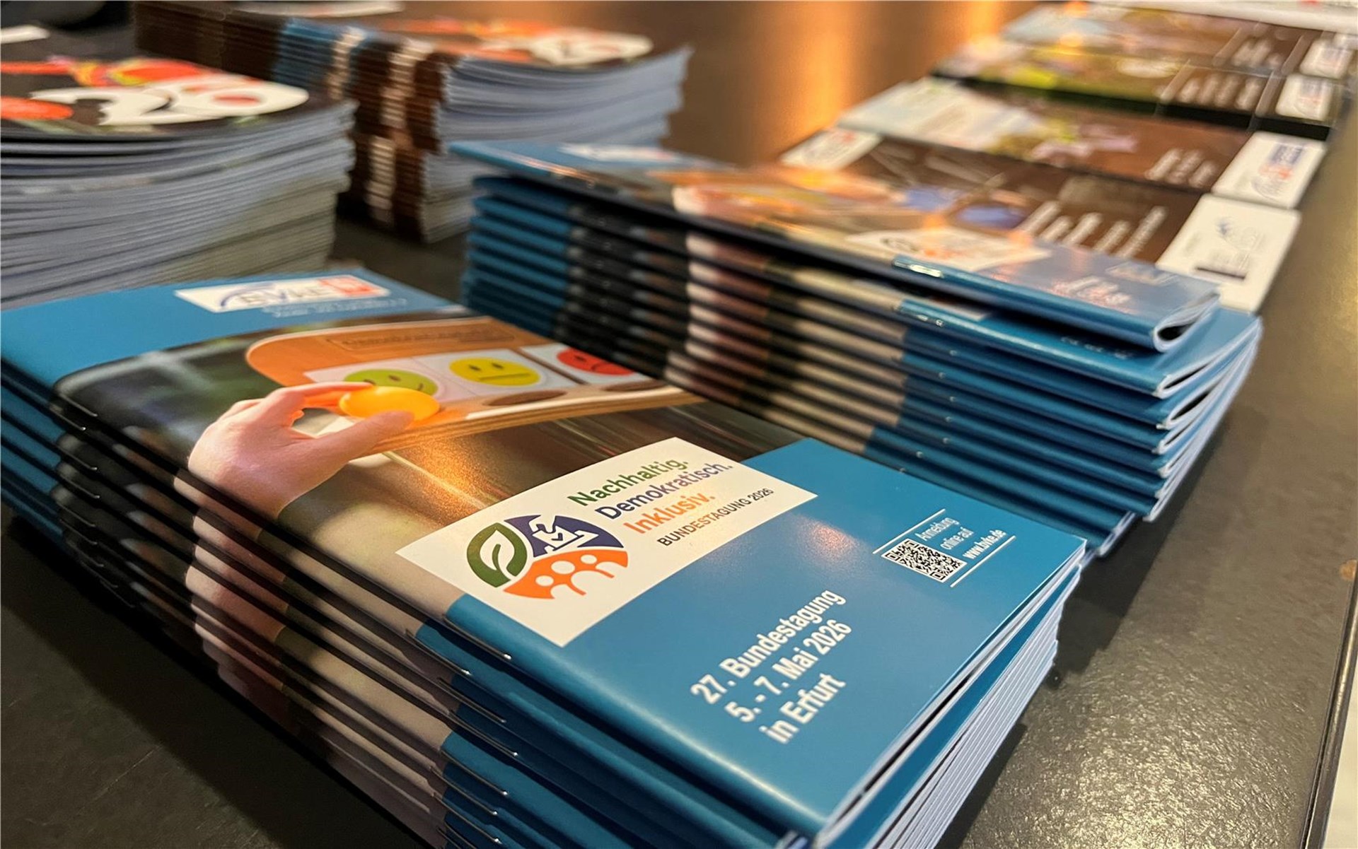 Stapel von Broschüren mit dem Titel "Nachhaltig Demokratisch Inklusiv" und Informationen über die 27. Bundestagung 2026 in Erfurt liegen auf einem Tisch.