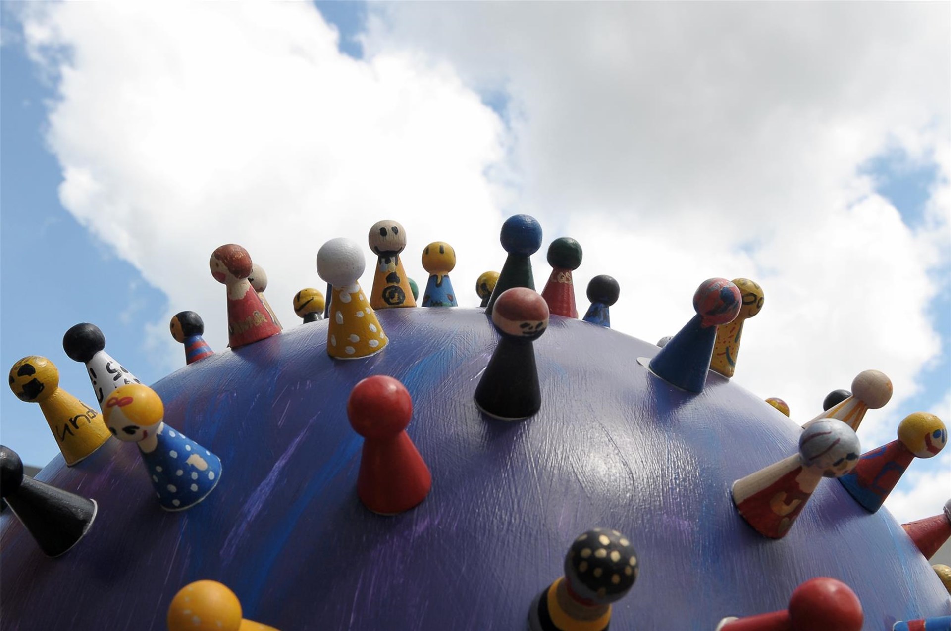 Das Bild zeigt bunt bemalte Spielfiguren, die auf einer runden, kugelförmigen Fläche stehen und so eine Gemeinschaft auf einer Weltkugel symbolisieren.