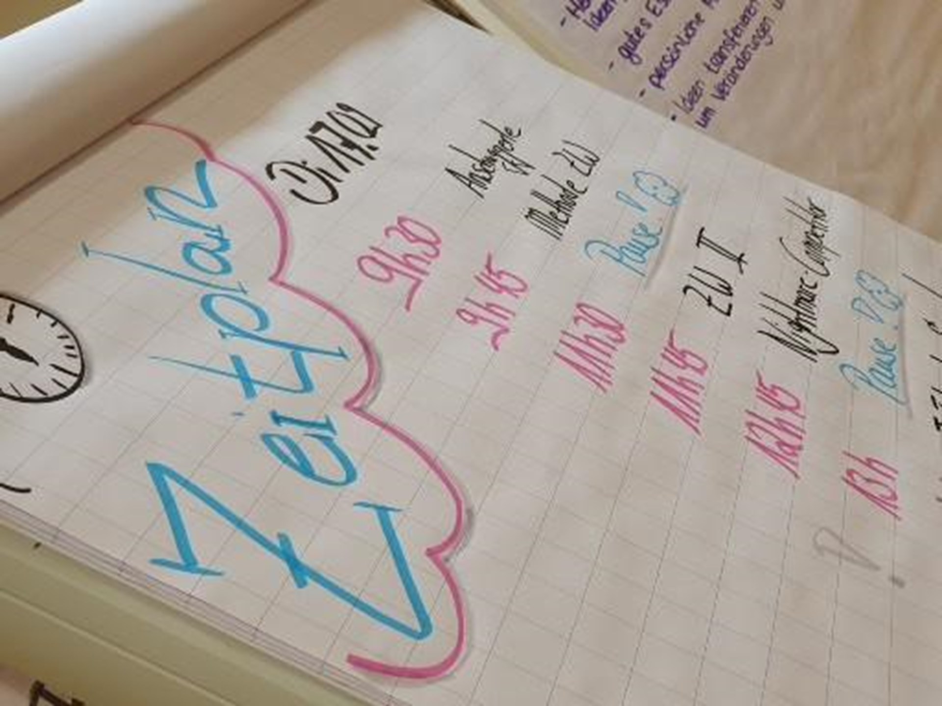Ein Notizblock mit handschriftlichem Zeitplan, der Termine und Uhrzeiten in blauer und roter Schrift zeigt.